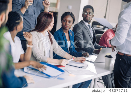 Mixed race people listening to presentation sitting in row at boardroom table 48075711