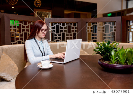 Business woman working at hotel lobby with laptop and drinking coffee Business woman working at hotel lobby with laptop and drinking coffee 48077901