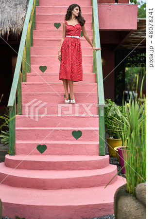 Brunette woman in red dress posing on colorful vintage stair outdoors 48078241