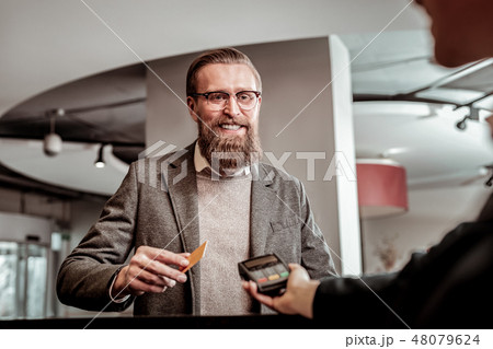 Positive delighted bearded male person paying for room 48079624