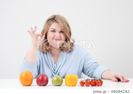 Young curvy fat woman in casual blue clothes on a white background at the table and shows OK Young curvy fat woman in casual blue clothes on a white background at the table and shows OK 48084282