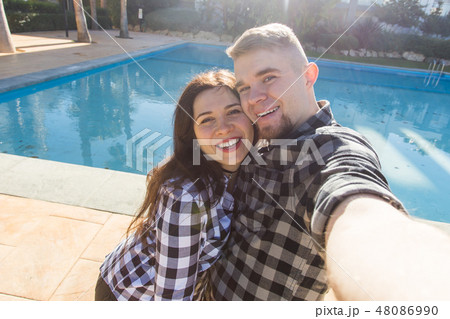 Travel, vacation and holiday concept - Young couple selfie smartphone photo near a swimming pool. Travel, vacation and holiday concept - Young couple selfie smartphone photo near a swimming pool. 48086990