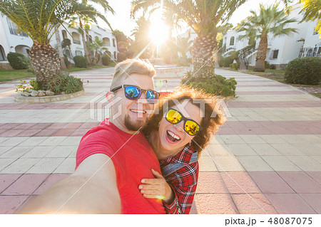 Travel, vacation and holiday concept - Happy couple having fun taking selfie over park with palms 48087075