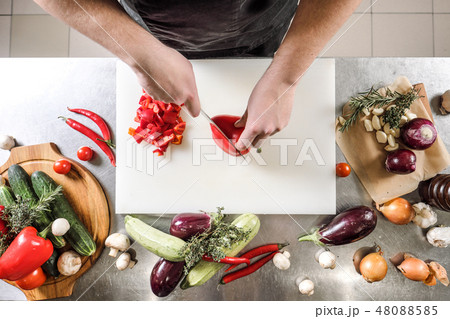 Male chef cuts vegetables for salad in a restaurant in a black apron. White cutting board, closeup Male chef cuts vegetables for salad in a restaurant in a black apron. White cutting board, closeup 48088585