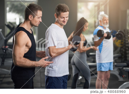 People working out in gym with personal trainers. 48088960