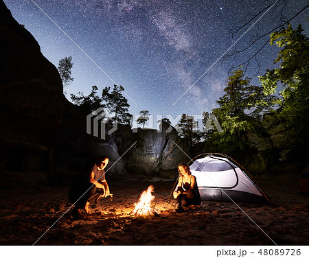 Couple tourists resting beside camp, campfire tent at night Couple tourists resting beside camp, campfire tent at night 48089726