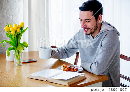 man sitting at table with cup of coffee or tea and eating croissant. man sitting at table with cup of coffee or tea and eating croissant. 48094097