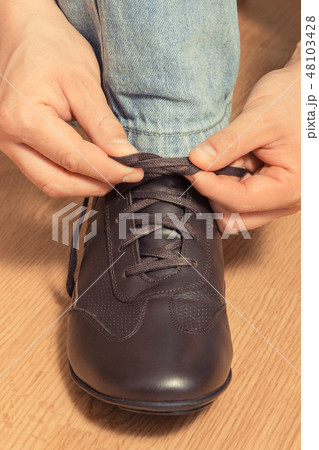 Hands tying shoelaces of brown leather shoe 48103428
