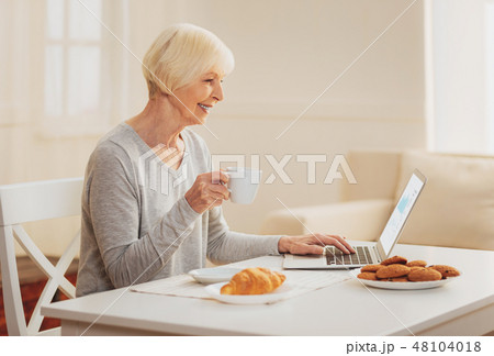 Woman checking e-mail while drinking tea in the kitchen Woman checking e-mail while drinking tea in the kitchen 48104018