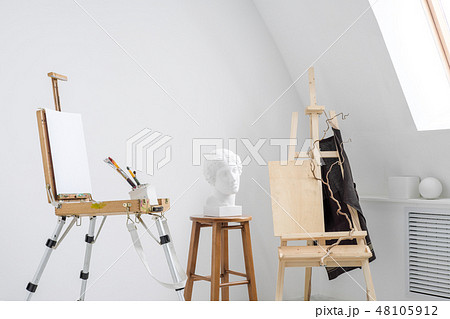 White and bright studio with a window. Workspace of the artist. Easel, canvases and plaster figures White and bright studio with a window. Workspace of the artist. Easel, canvases and plaster figures 48105912