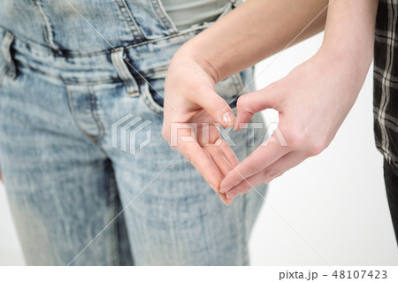 Two girls in jeans hold hands close up. White background. Homosexual lesbian couple. Two girls in jeans hold hands close up. White background. Homosexual lesbian couple. 48107423