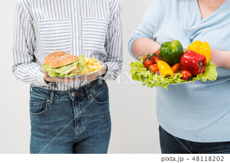 Two girls, thick and thin, with healthy food from vegetables and fruits and unhealthy fast food with Two girls, thick and thin, with healthy food from vegetables and fruits and unhealthy fast food with 48118202
