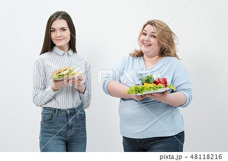 Two girls, thick and thin, with healthy food from vegetables and fruits and unhealthy fast food with 48118216