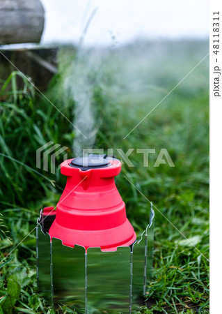 Fodable camping kettle with boiling water standing on burning stove. 48118311