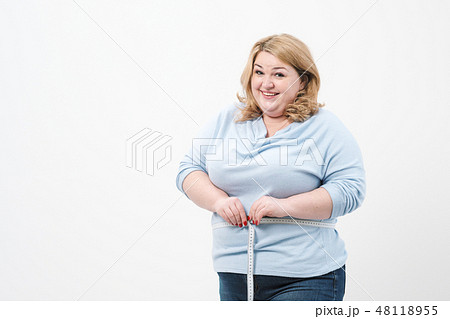 A fat woman measures her waist with a measuring tape in casual clothing on a white background. 48118955