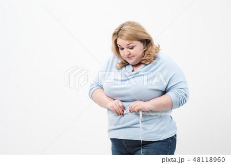 A fat woman measures her waist with a measuring tape in casual clothing on a white background. 48118960
