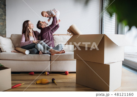 A portrait of young couple with a baby and cardboard boxes moving in a new home. 48121160
