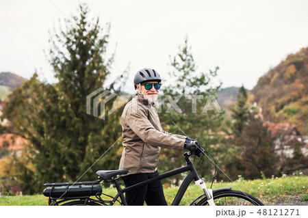 Active senior man with electrobike standing outdoors on a road in nature. Active senior man with electrobike standing outdoors on a road in nature. 48121271