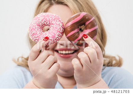 A fat, plump blonde woman on a white background, holding pink glazed donuts and a red apple. 48121703