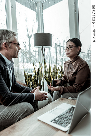Dark-haired elegant woman in a brown satin blouse speaking in the office with her partner 48127899