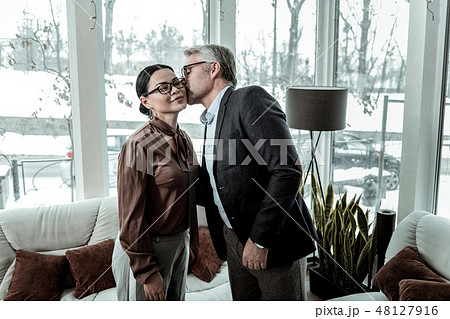 Tall grey-haired handsome man in a blue shirt kissing a woman on a cheek 48127916