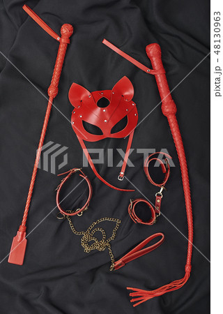 Couple Sexy Toys. Vertical photo of red bdsm leather set (handcuffs, whip, mask, chain) on a black 48130963