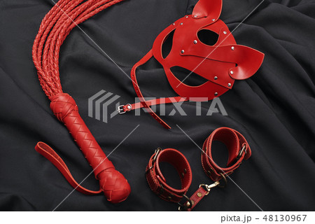 BDSM Sexual Practice. Top view of red bdsm leather set (handcuffs, whip, mask) on a black silk BDSM Sexual Practice. Top view of red bdsm leather set (handcuffs, whip, mask) on a black silk 48130967