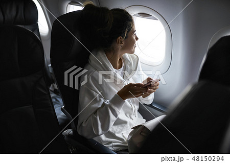 Woman with smartphone sits on black seat in plane 48150294