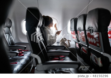Woman with smartphone sits on black seat in plane 48150296