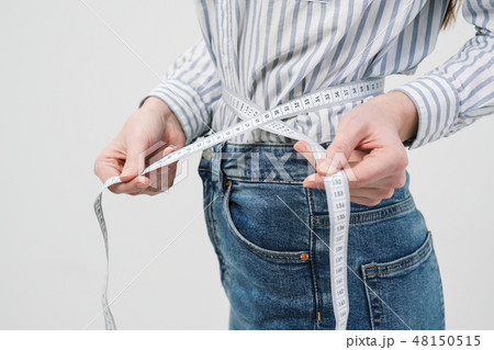 Young slim slim girl measures the waist tape in jeans and shirt on a white background. 48150515