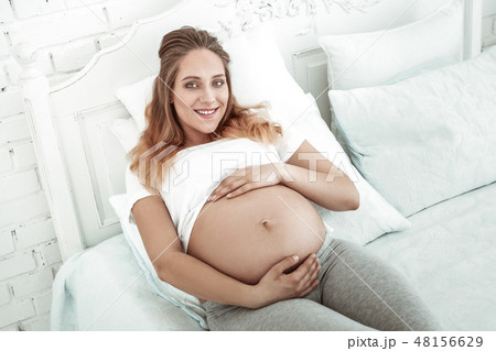 Pleasant woman with wide smile wrapping pregnant belly Pleasant woman with wide smile wrapping pregnant belly 48156629