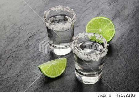 A photo of a tequila shots with lime slices on a black background with copy space 48163293