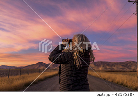 Woman using binoculars at sunset 48175387