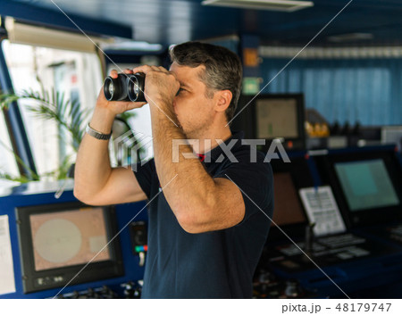 Officer during navigational watch looking through binoculars Officer during navigational watch looking through binoculars 48179747