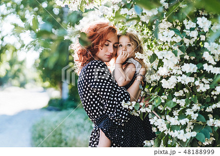 Young woman stands near jasmine with a small daughter Young woman stands near jasmine with a small daughter 48188999