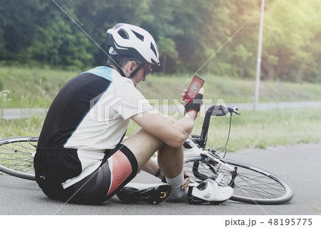 Injured biker holding smartphone calling rescue Injured biker holding smartphone calling rescue 48195775