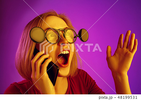 Portrait of surprised confused woman with mobile phone isolated over neon background 48199531