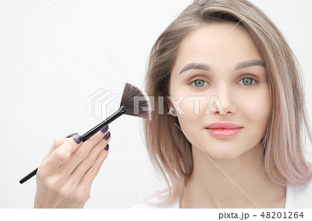 Make-up artist makes makeup beautiful blonde girl on a white background. Close-up hands with brush 48201264