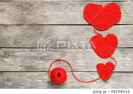 Three red knitted hearts on a gray wooden back Three red knitted hearts on a gray wooden back 48208419