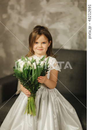 Beautiul little girl hold a bouquet of flowers at home. She sist on sofa at home and waiting for her 48212691