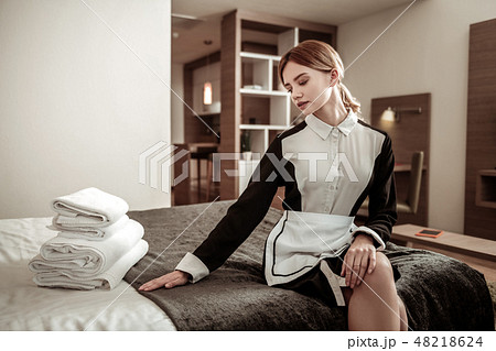Young housekeeper wearing uniform sitting on nice big bed Young housekeeper wearing uniform sitting on nice big bed 48218624