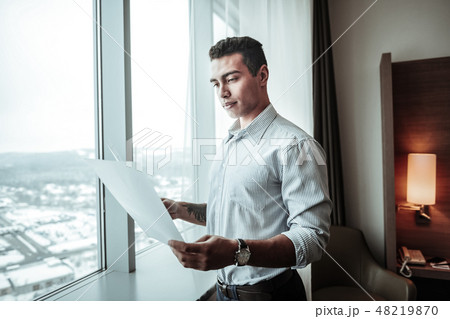 Young ceo holding some documents standing near window Young ceo holding some documents standing near window 48219870