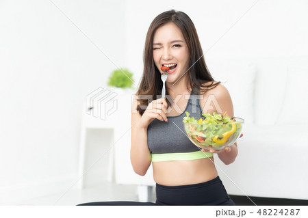 Young Asian woman is resting and eating a healthy salad after a 48224287