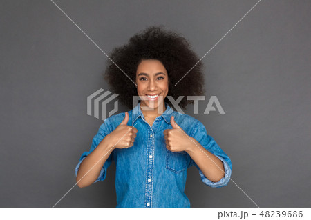 Freestyle. Mulatto woman standing isolated on grey showing thumbs up smiling cheerful Freestyle. Mulatto woman standing isolated on grey showing thumbs up smiling cheerful 48239686
