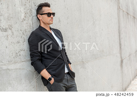 Outdoors leisure. Young man in suit and sunglasses on city street isolated leaning on wall serious Outdoors leisure. Young man in suit and sunglasses on city street isolated leaning on wall serious 48242459
