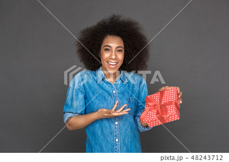 Freestyle. Mulatto woman standing isolated on grey pointing at present smiling surprised 48243712