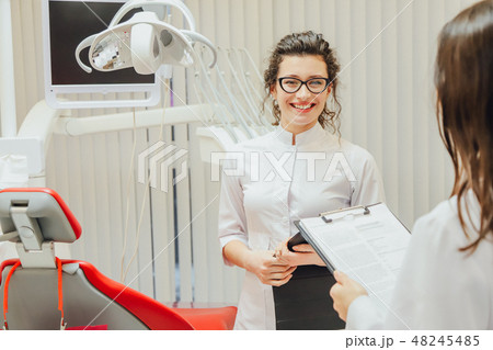 Portrait of a smiling dentist and assistant, looking at the clipboard in a modern dental clinic 48245485