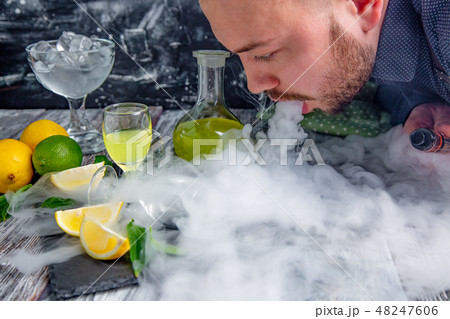 man lets out steam from a mouth on a table served with limoncello man lets out steam from a mouth on a table served with limoncello 48247606