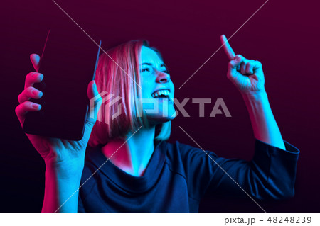 Portrait of a confident casual girl showing blank screen mobile phone isolated over blue background 48248239
