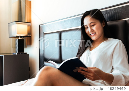 woman sitting on bed reading the book 48249469